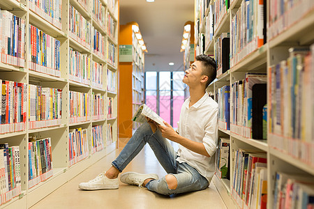 坐在图书馆书架旁看书的男生图片