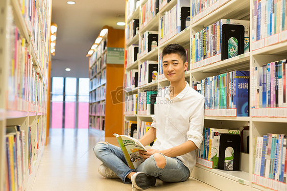 坐在图书馆书架旁看书的男生