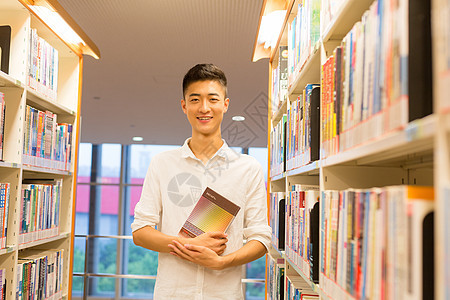 站在图书馆书架旁看书的帅气男同学背景图片