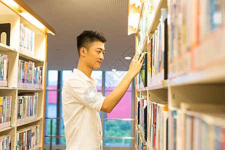 男生在图书馆书架旁选看图书图片