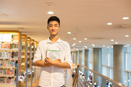 站在图书馆书架旁看书的帅气男同学背景图片