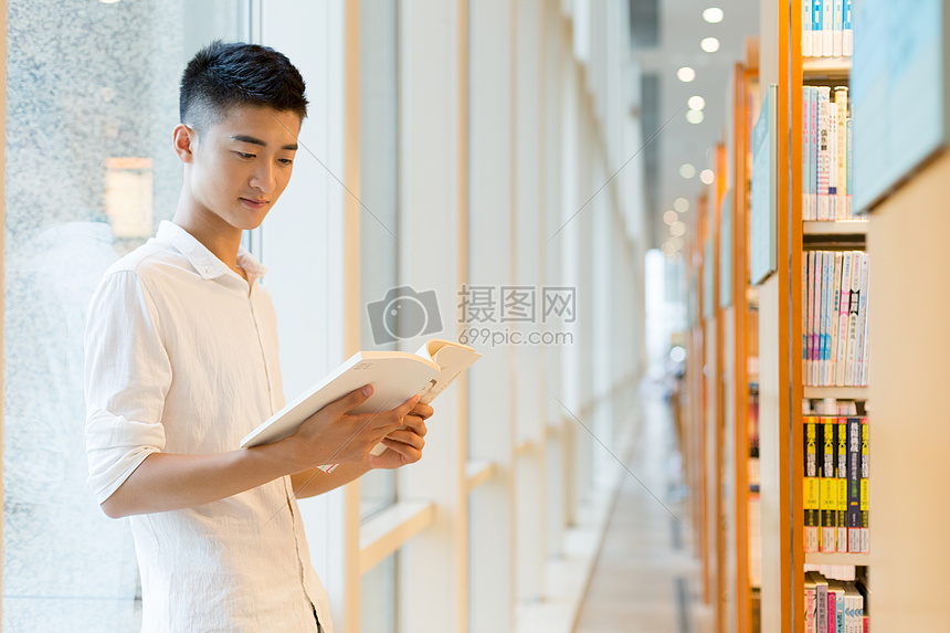 站在图书馆书架旁看书的帅气男同学图片