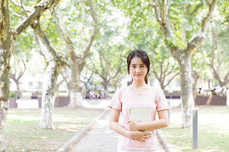 学生读书拿着书站在校园林荫道上的女生背景