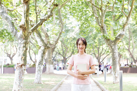 拿着书站在校园林荫道上的女生图片