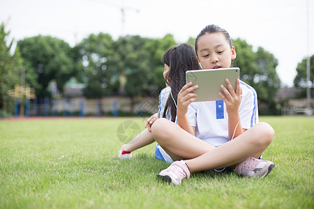 学生学习坐在草坪上使用平板电脑的小学生背景