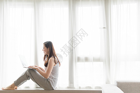 落地飘窗坐在窗台使用电脑休闲放松的女性背景