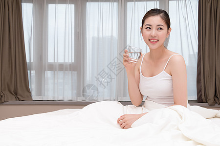 早起睡前坐在床上喝水的美女图片