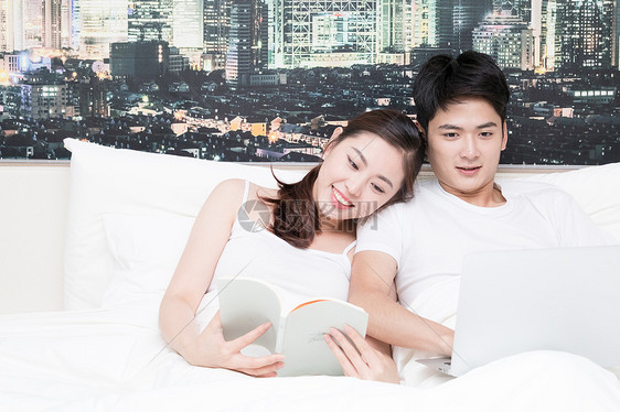 情侣一起坐在床上看书使用电脑图片