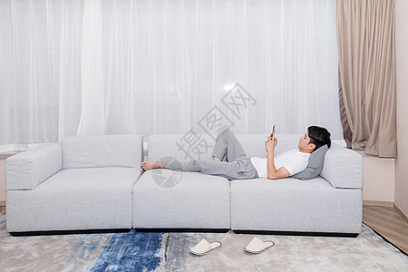 男生躺在沙发上玩手机购物图片