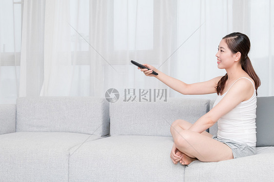 坐在沙发上拿着遥控器看电视的年轻女性图片