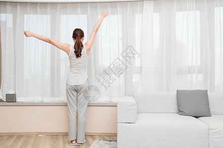 明亮早起年轻女性在客厅窗前伸展运动背景