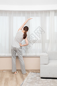 年轻女性在客厅窗前伸展运动图片