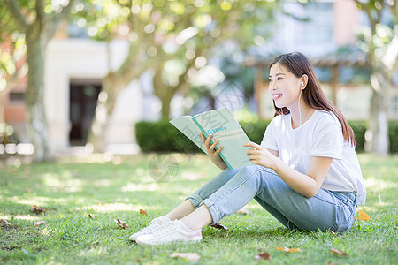 坐在校园草坪上看书的女学生背景图片