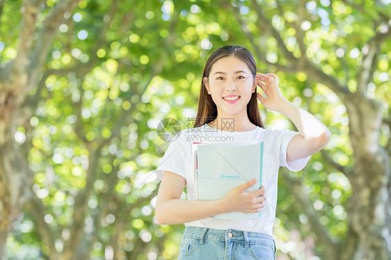 校园林荫道上微笑看书的学生图片