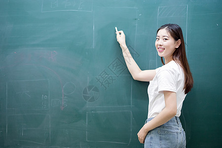 拿着粉笔站在黑板面前的老师背景图片