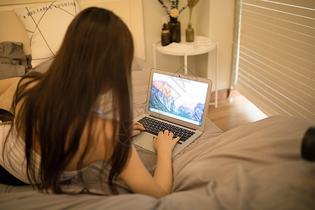 躺在床上玩电脑的年轻女性背景图片