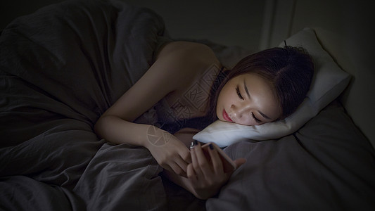 深夜睡前躺着玩手机的女生背景