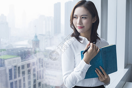 女白领在落地窗前站立：商务办公的成功人士背景图片