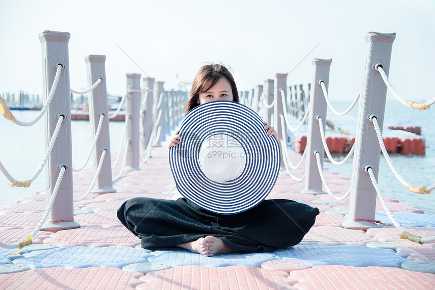 海边渔港旁坐着拿着草帽的女模特图片