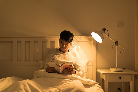 坐在床上看书晚上坐在床头看书的年轻男性背景