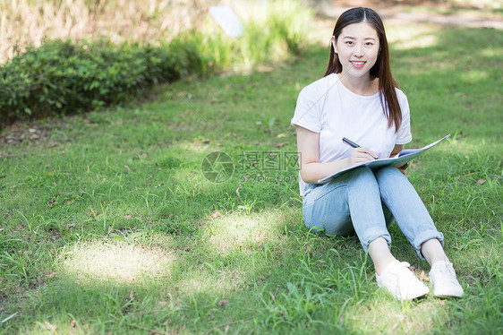 拿着课本坐在草坪上看书的大学生图片