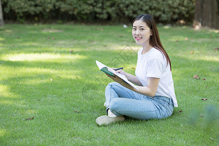 拿着课本坐在草坪上看书的大学生图片