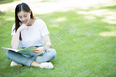 拿着课本坐在草坪上看书的大学生图片