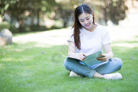 拿着课本坐在草坪上看书的大学生图片