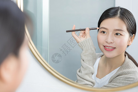 站在镜子前画眉的年轻女性图片