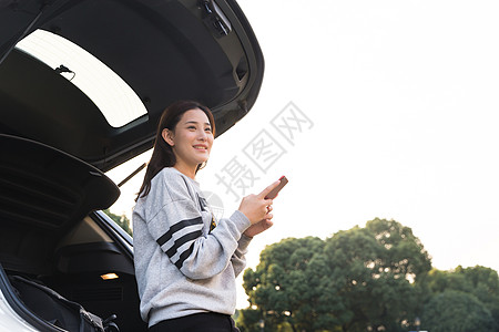 美女在后备箱拿着手机看远方高清图片