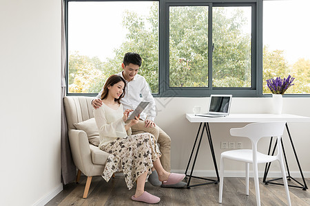 年轻夫妻幸福地坐在沙发上看平板电脑图片