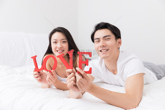 年轻夫妻开心躺床上手拿LOVE图片