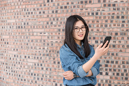 站在墙前的年轻女性用手机图片