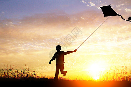 黄昏草地黄昏下放风筝的男孩设计图片