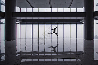 落地玻璃前跳跃的男子剪影图片