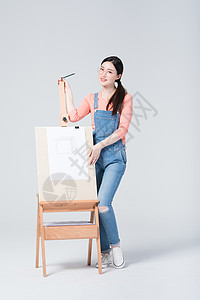 青年美女手拿铅笔站在画架旁图片
