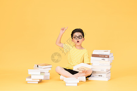 孩子书拿着书本坐在书旁的快乐男孩背景