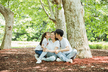 父母亲吻孩子一家人坐在大树下休息背景