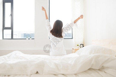 白色被子年轻女性坐床边伸展背影背景