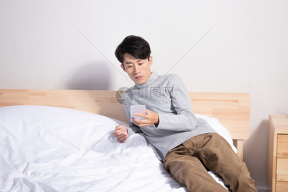 躺在床上玩手机的男性图片