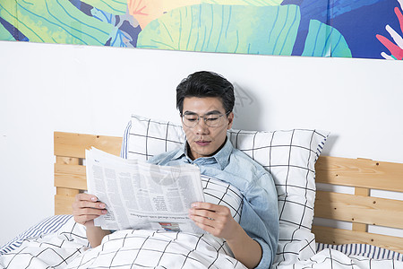 青年男性床上看报纸背景图片