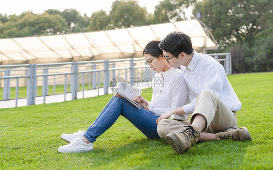 青年情侣坐在公园草地上看书图片