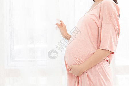 一个孕妇在客厅站着抚摸肚子高清图片
