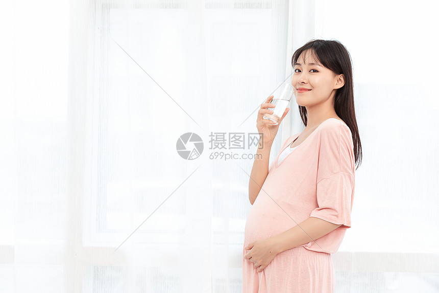 一个孕妇站着在客厅喝水图片
