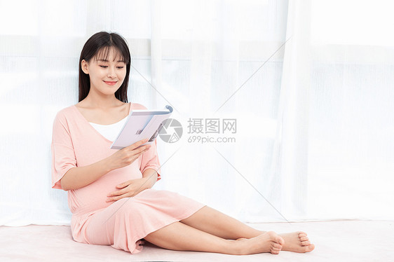 孕妇在纱窗旁边侧腿坐着看书阅读图片