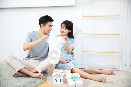 丈夫给孕妇展示自己给孩子买的婴儿衣服图片