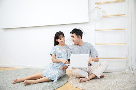 孕妇和丈夫一起在卧室地毯上看电脑背景
