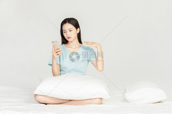 女性坐在床上玩手机图片