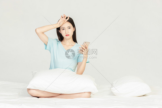 女性坐在床上玩手机图片