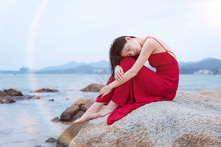 花裙子少女坐在深圳较场尾海边礁石上的红衣少女背景